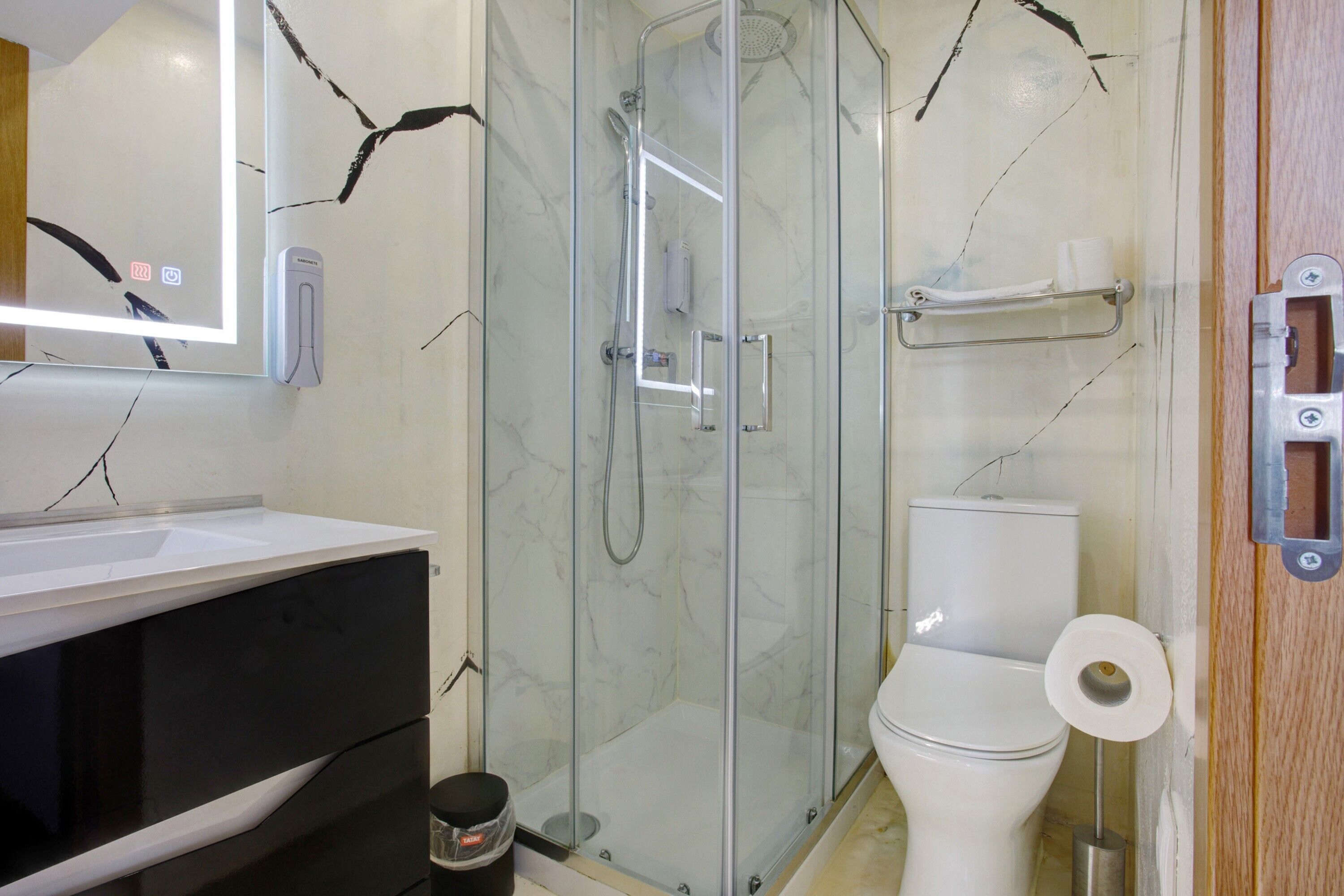Ein Badezimmer mit einer gläsernen Duschkabine, Toilette, Waschbecken mit Spiegel und Handtuchhalter.
