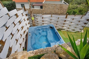 A hot tub surrounded by a wooden fence, with a stone building and greenery in the background. - Holiday Home 'Castelos Azul' with Private Garden, Wi-Fi and Air Conditioning (Ourém)