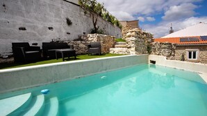 Una piscina con un muro de piedra, asientos exteriores y cielo despejado.