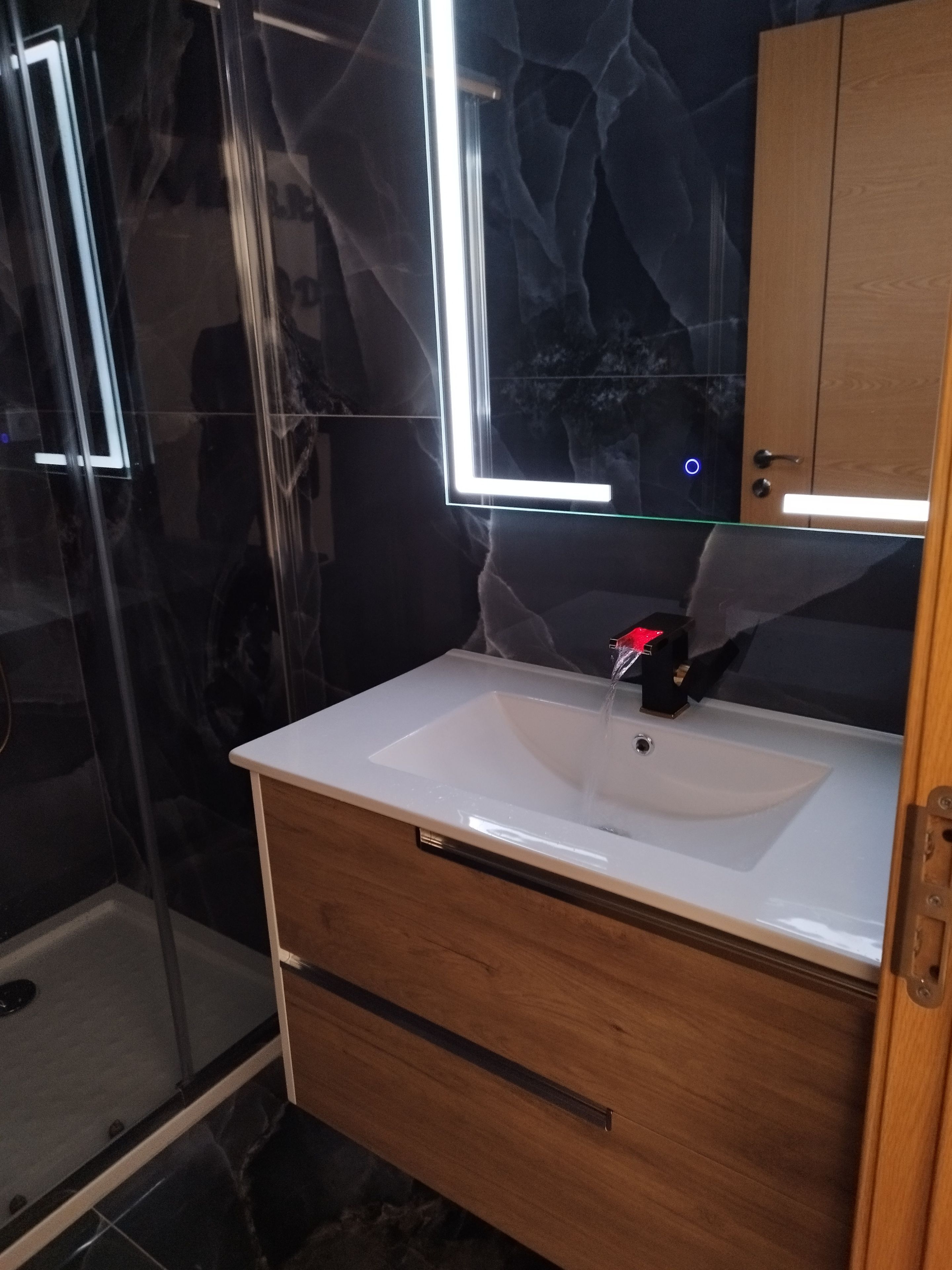 Ein Badezimmer mit Waschbecken, Holzschrank und einer Duschkabine aus Glas.