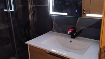 Ein Badezimmer mit Waschbecken, Holzschrank und einer Duschkabine aus Glas.