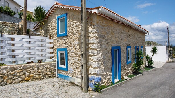 Un bâtiment en pierre avec des fenêtres et des portes à cadre bleu, un chemin pavé et une clôture blanche.