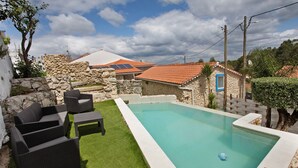 Une piscine avec un mur en pierre et un petit bâtiment doté d’une porte bleue.
