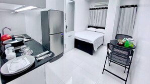 A compact hotel room with a kitchenette, a bed, a small table with a chair, and a ceiling fan. - 250 sqft 2 Studio Apt Pool and Sauna (Dhaka)