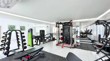 Ein Fitnessraum mit unterschiedlichen Trainingsgeräten, darunter Kurzhanteln, eine Trainingsbank und Kraftgeräte.