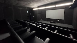 A dark, dimly lit movie theater with rows of black seats, a large screen, and a stage area with audio equipment. - 250 sqft 2 Studio Apt Pool and Sauna (Dhaka)