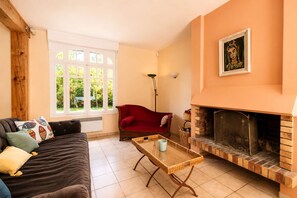 A living room with a sofa, a red chair, a fireplace, and a window with a view of greenery.