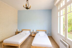 A room with two wooden beds, a brick wall, a blue wall, and a window with a view of greenery.