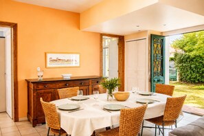 A dining area with a table set for four, surrounded by wicker chairs, a wooden cabinet, and a framed picture on the wall.