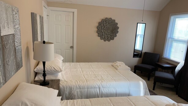 A hotel room with two beds, a desk, a chair, and a decorative wall piece.