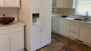 A kitchen with white cabinets, a white refrigerator, a sink, and a window with blinds.