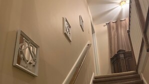 A carpeted staircase with a handrail, beige walls, and a light fixture at the top.
