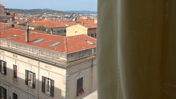 Vista de un paisaje urbano a través de una ventana, con una cortina que cubre parcialmente la vista.