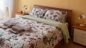 Una cama bien hecha con ropa de cama floral, una lámpara de noche y un cuadro en la pared.