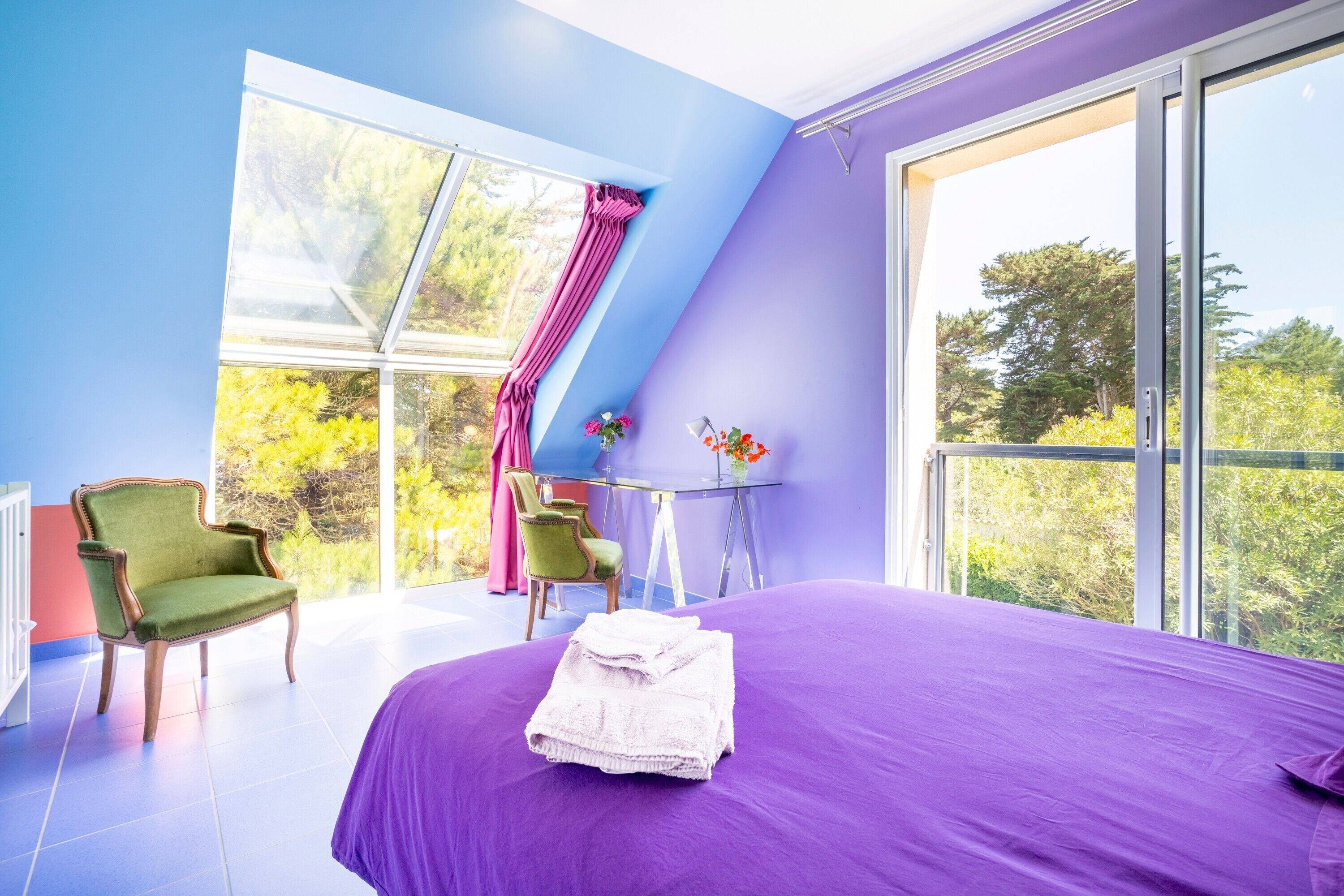A bedroom with a large bed, a chair, a small table, and a window with a view of trees.