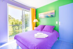 Una habitación con una cama, un cuadro, una lámpara y vistas por una ventana.
