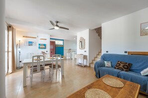 Una sala moderna con un sofá azul, una mesa de centro de madera y un comedor con una mesa y sillas blancas.