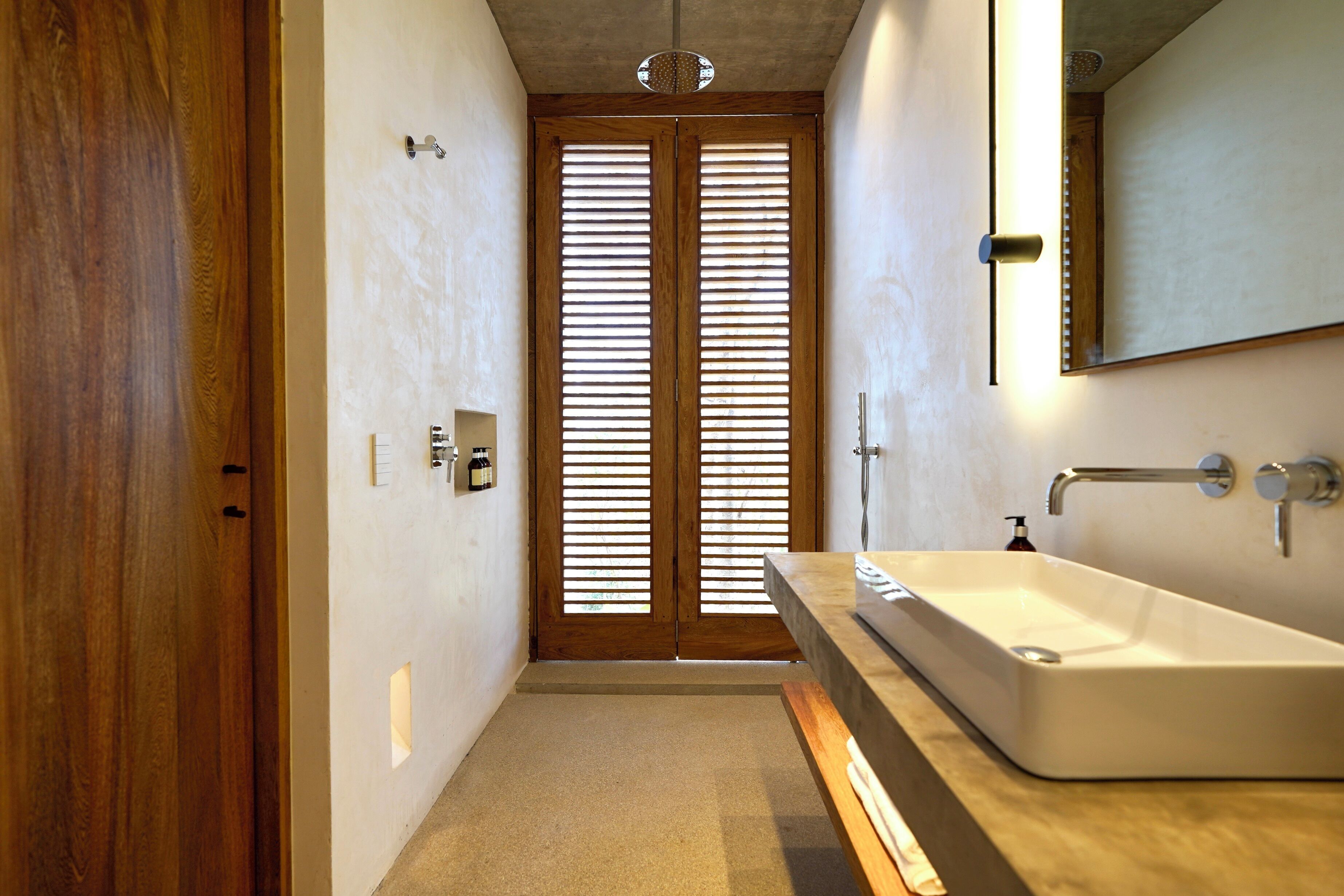 A modern bathroom with a wooden door, a large mirror, and a white sink.