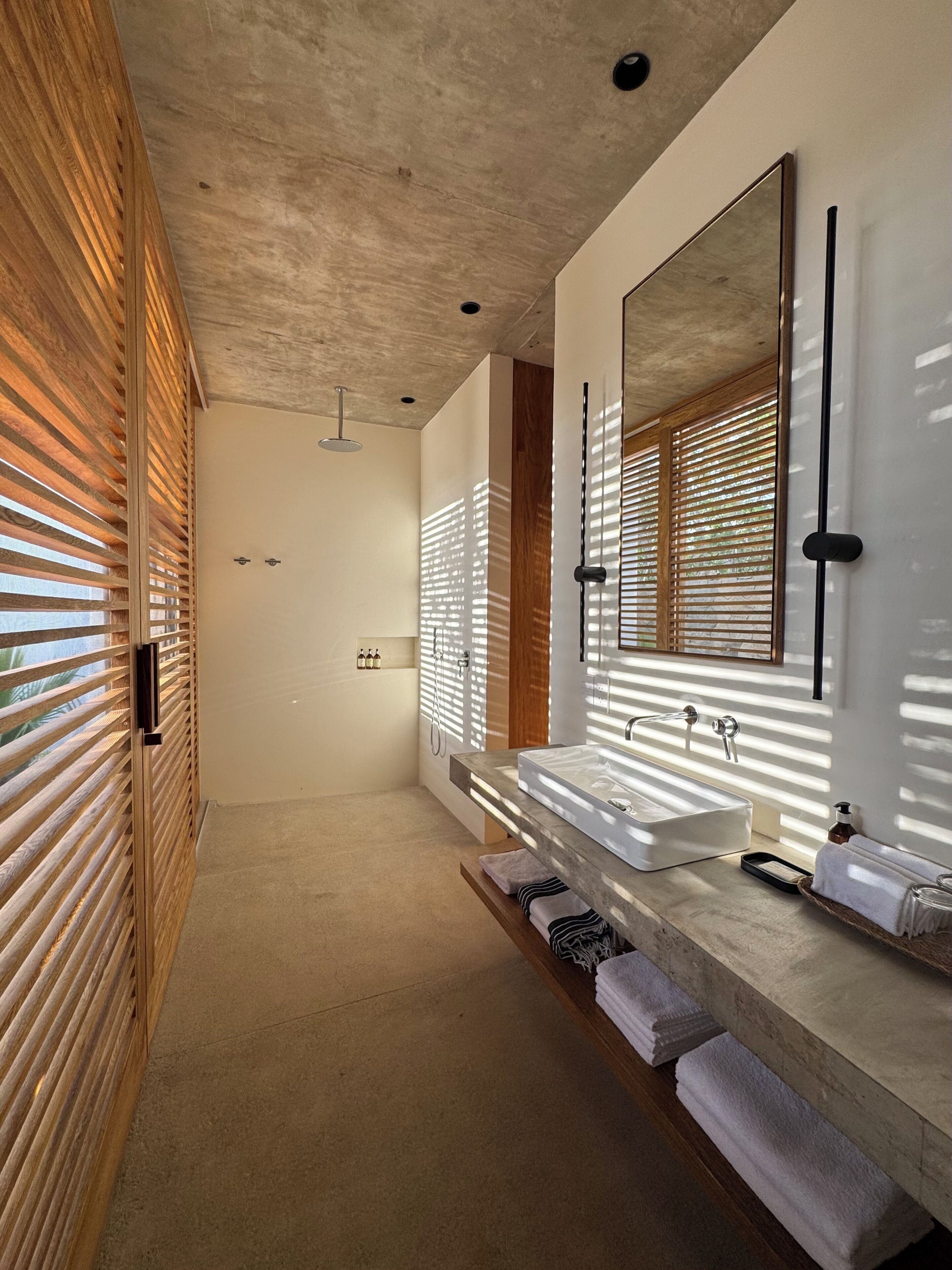 A modern bathroom with a large mirror, two sinks, and wooden blinds.