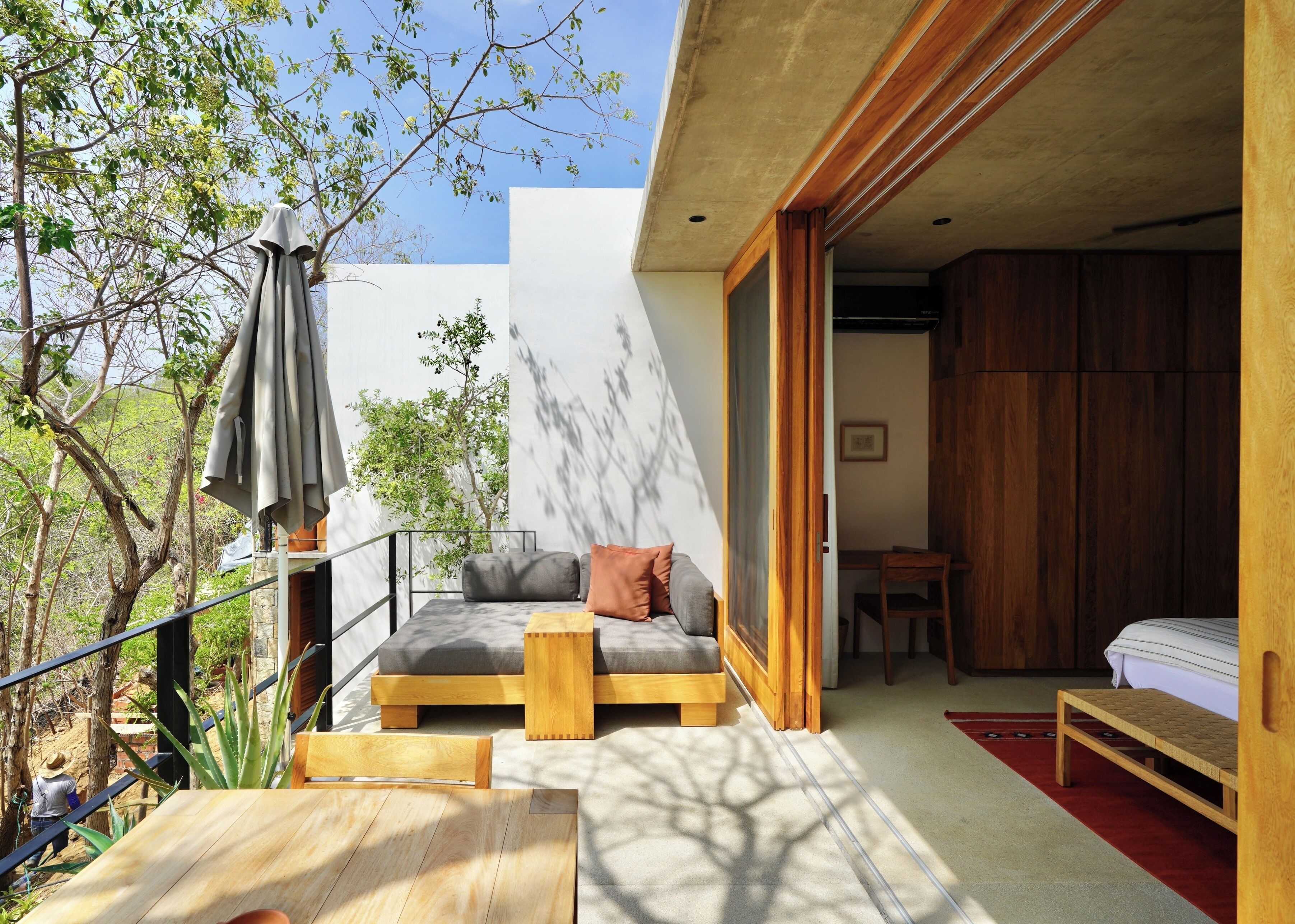 A modern outdoor seating area with a wooden table and chairs, a cushioned bench, and a patio umbrella.