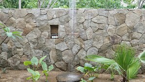 A stone wall with a water feature, a small window, and tropical plants. - El Guayacan  (Santa Maria Tonameca)