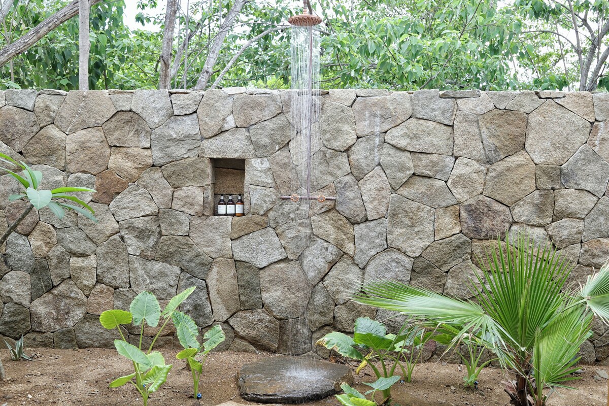 A stone wall with a water feature, a small window, and tropical plants.