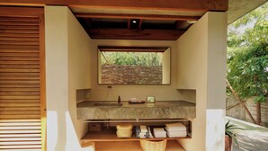 A bathroom with a stone sink, a mirror, and a window with a view of greenery. - El Guayacan  (Santa Maria Tonameca)