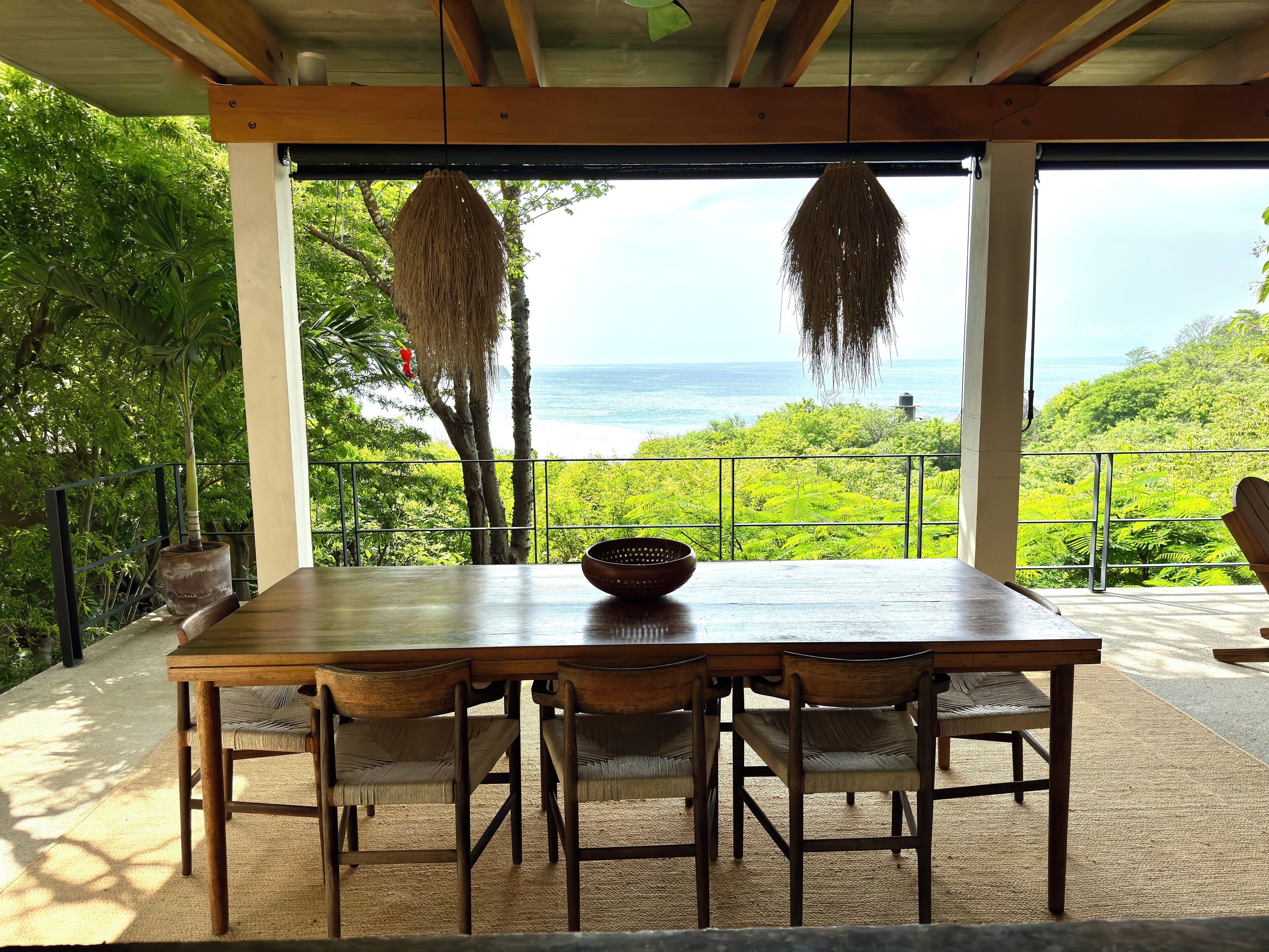 A wooden table with chairs, a woven basket, and a view of the ocean through a balcony.