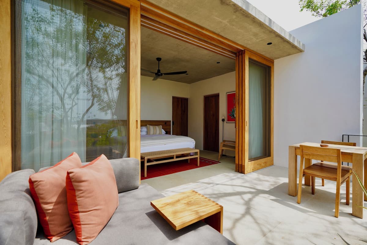 A modern bedroom with a bed, wooden furniture, and large windows.