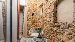 Un muro de piedra, sillas de mimbre blanco y una planta en maceta en un patio.
