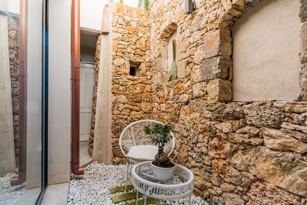 A stone wall, white wicker chairs, and a potted plant in a courtyard.