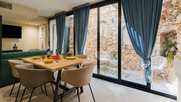 Comedor con una mesa, sillas y vistas a un muro de piedra y asientos exteriores.