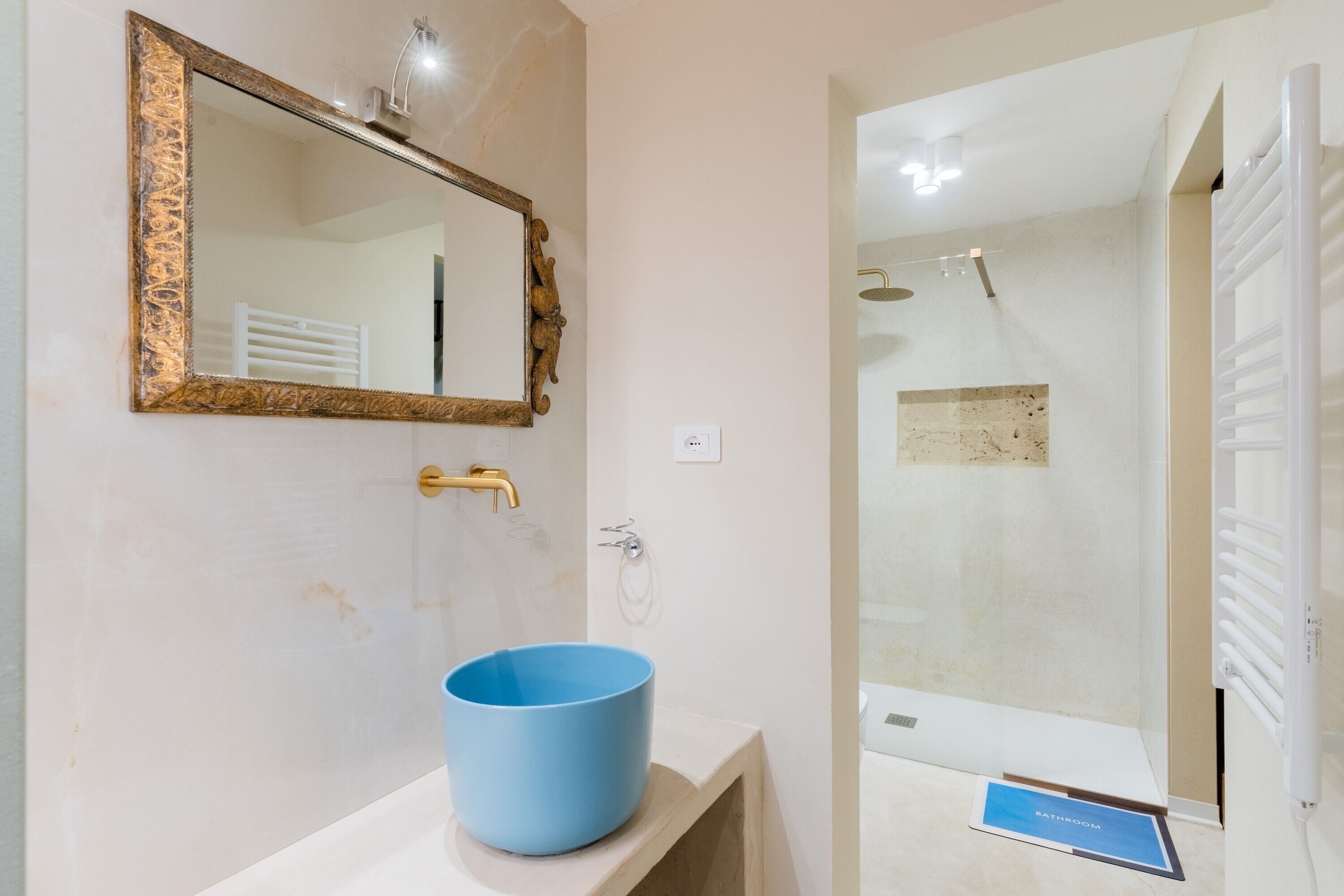 Un bagno con un lavandino blu, uno specchio con cornice dorata e una doccia.