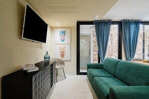 Ein modernes Wohnzimmer mit einem Flachbildfernseher, einem grünen Sofa, einer schwarzen Kommode und zwei gerahmten Kunstwerken an der Wand.