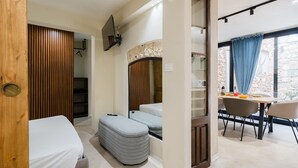 Una habitación compacta con cama, zona de estar con mesa y sillas, espejo y ventana con cortinas.