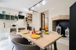 A modern kitchen with a dining table set for two, a microwave, a coffee machine, and a black TV on the wall.