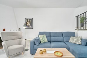 Un salon avec un canapé bleu, un fauteuil gris, une table basse en bois et un lampadaire.