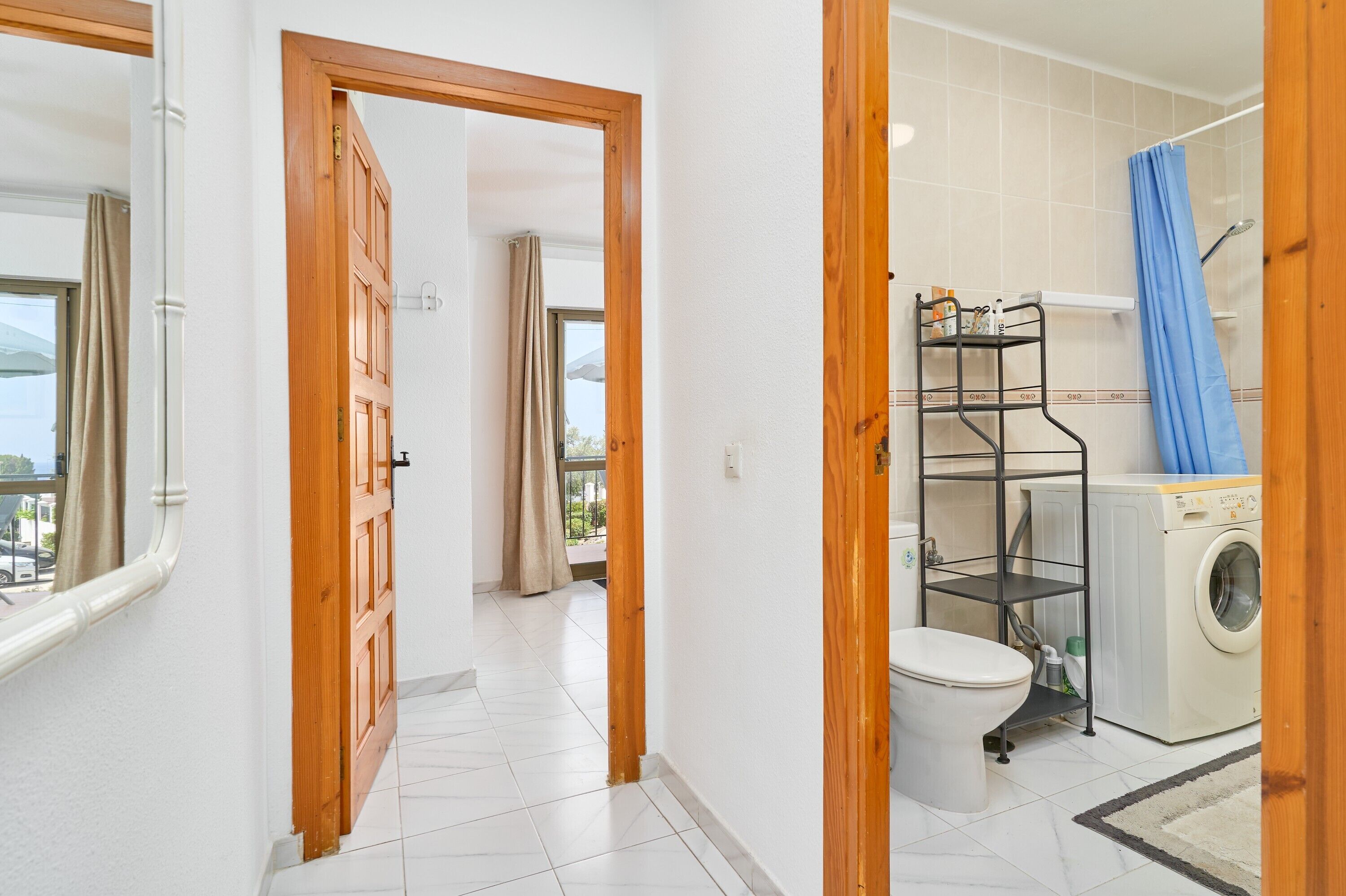 A bathroom with a washing machine, a shelf with toiletries, and a view through an open door.