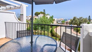 A balcony with a glass table, a black umbrella, and a view of a coastal town. - Holiday Home 'Casa Andalusia' with Sea View, Wi-Fi and Air Conditioning (Nerja)
