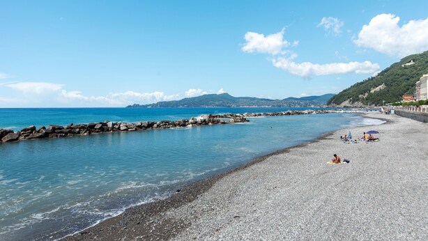 A pebble beach with clear water, a rocky breakwater, and distant mountains. - Queta – Modern Apartment: Comfort, Sea & City Center on Foot (Chiavari)