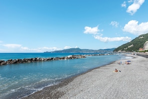 A pebble beach with clear water, a rocky breakwater, and distant mountains.