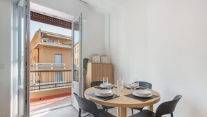 A dining area with a round table, black chairs, and a view of a building through an open door. - Queta – Modern Apartment: Comfort, Sea & City Center on Foot (Chiavari)
