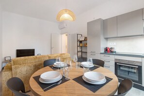 A modern dining area with a round table set for four, a sofa, and a kitchen with a built-in oven. - Queta – Modern Apartment | Comfort, Beach & City Center on Foot (Chiavari)