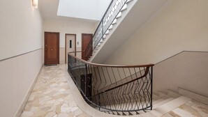 A curved staircase with a metal railing, a stone-patterned floor, and a ceiling light. - Queta – Modern Apartment: Comfort, Sea & City Center on Foot (Chiavari)