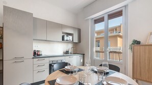 A modern kitchen with white cabinets, a microwave, and a dining area with a round table set for four. - Queta – Modern Apartment: Comfort, Sea & City Center on Foot (Chiavari)