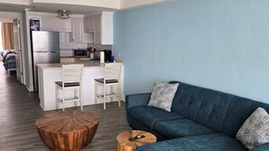 Una sala de estar moderna con un sofá azul, una mesa de centro de madera y una cocina al fondo.