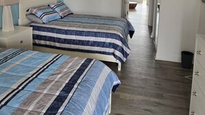 Un dormitorio con dos camas, una mesita de noche, un aparador y una puerta que da a un balcón.