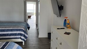 Un dormitorio con dos camas, un aparador, un televisor y vistas a un balcón.