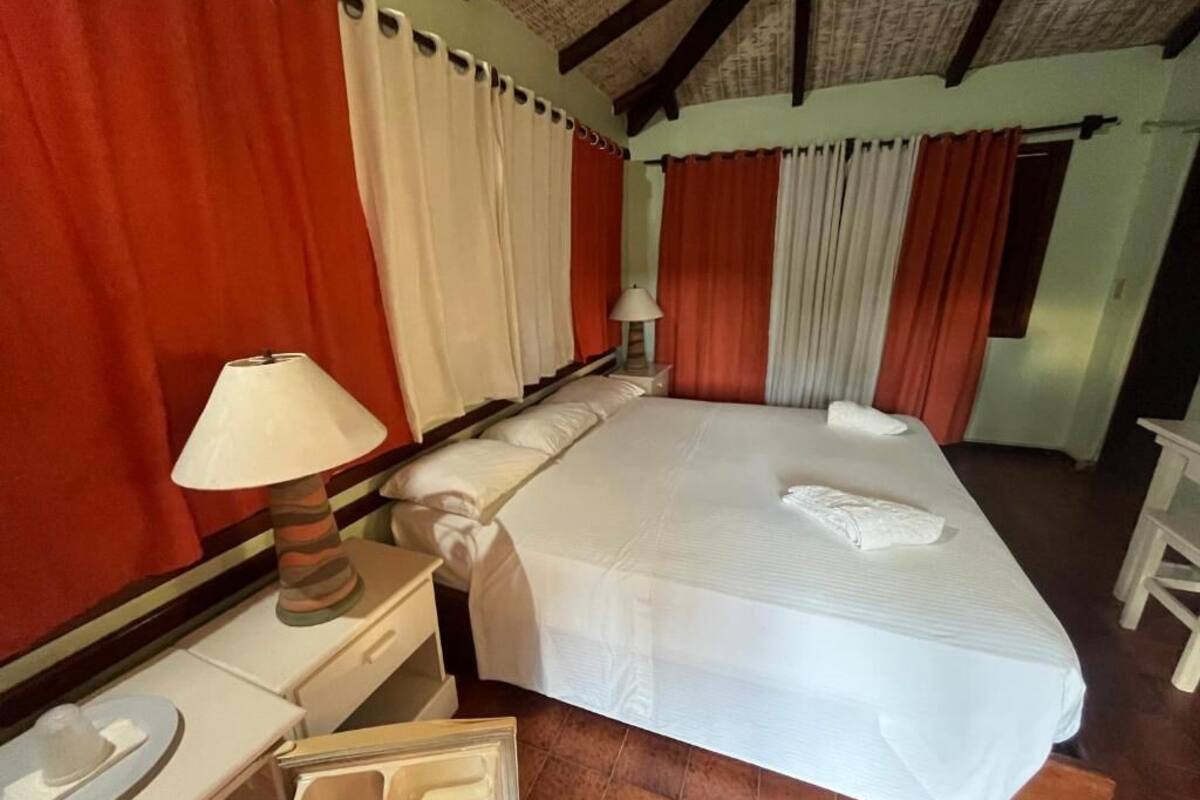 Un dormitorio con una cama grande, una mesita de noche con lámpara y cortinas.