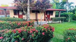 A building with a red roof, a porch with chairs, and a well-maintained garden with red flowers. - hotel palococo (Las Terrenas)